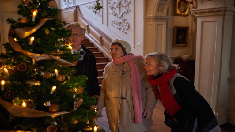 Three visitors looking at a Christmas tree in the Entrance Hall at Mompesson House, Wiltshire